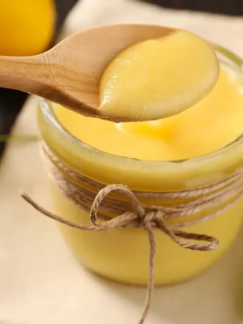Glas mit cremigem Zitronen-Curd, ein Holzlöffel voll Curd darüber