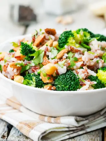 Eine Schale mit frischem Brokkoli-Reis-Salat, garniert mit Mandeln und frischen Kräutern.