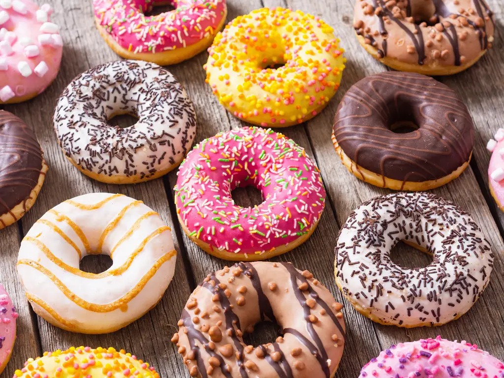 Bunte, glasierte Donuts mit verschiedenen Streuseln auf einem Holztisch