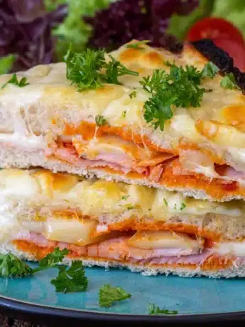 Gegrilltes Käsesandwich mit Schinken, überbacken mit Käse und garniert mit frischer Petersilie auf einem blauen Teller