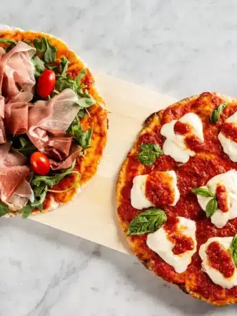 Zwei Pizzen mit glutenfreiem Pizzateig: eine mit Schinken, Rucola und Kirschtomaten und die andere mit Mozzarella und Basilikum