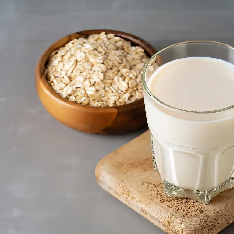 Ein Glas frische Hafermilch auf einem Holzbrett, daneben eine Schale mit Haferflocken.