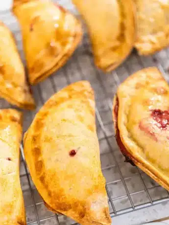 Mehrere frisch gebackene Obst-Empanadas, goldbraun und knusprig, auf einem Abkühlgitter.