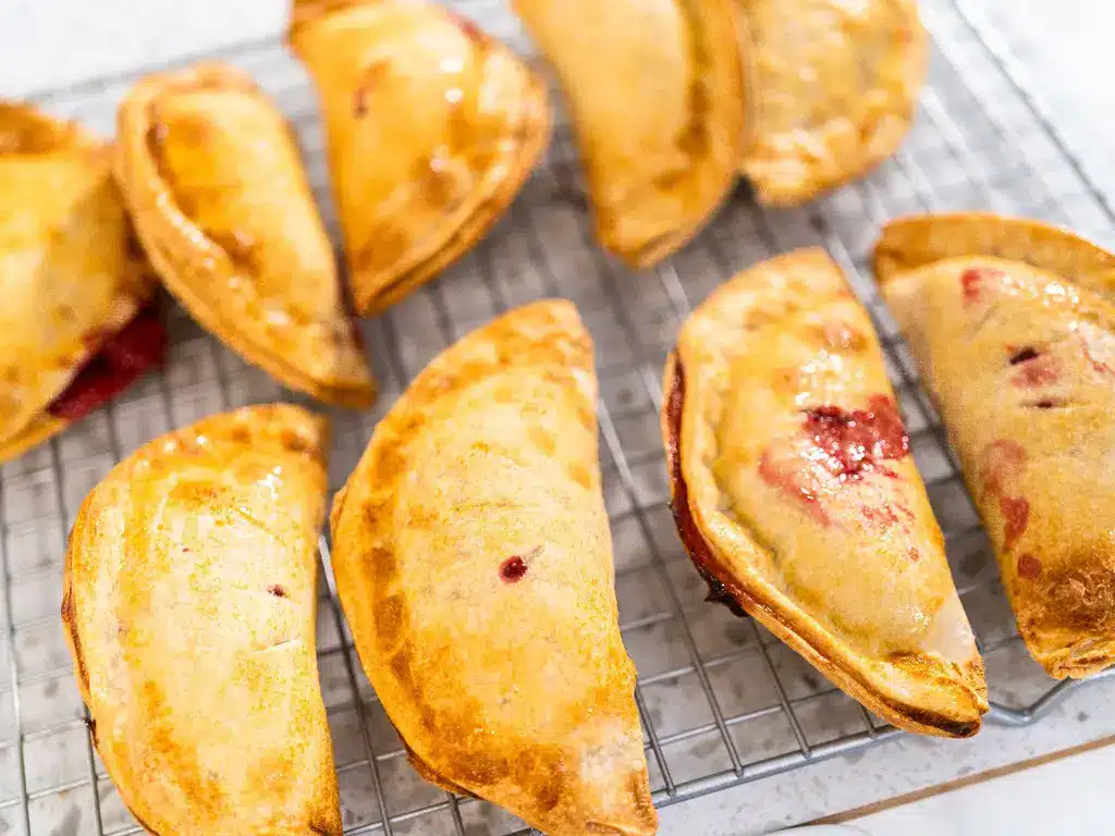 Mehrere frisch gebackene Obst-Empanadas, goldbraun und knusprig, auf einem Abkühlgitter.