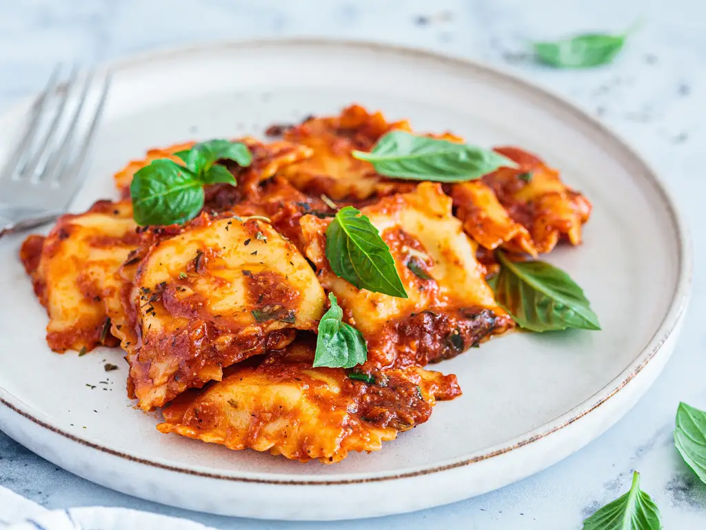 Teller mit Ravioli in Tomatensauce, garniert mit frischen Basilikumblättern