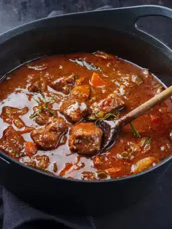 Ein Topf mit dampfendem Rindergulasch, zubereitet mit zarten Fleischstücken, Gemüse und Kräutern, in einer reichhaltigen Sauce.