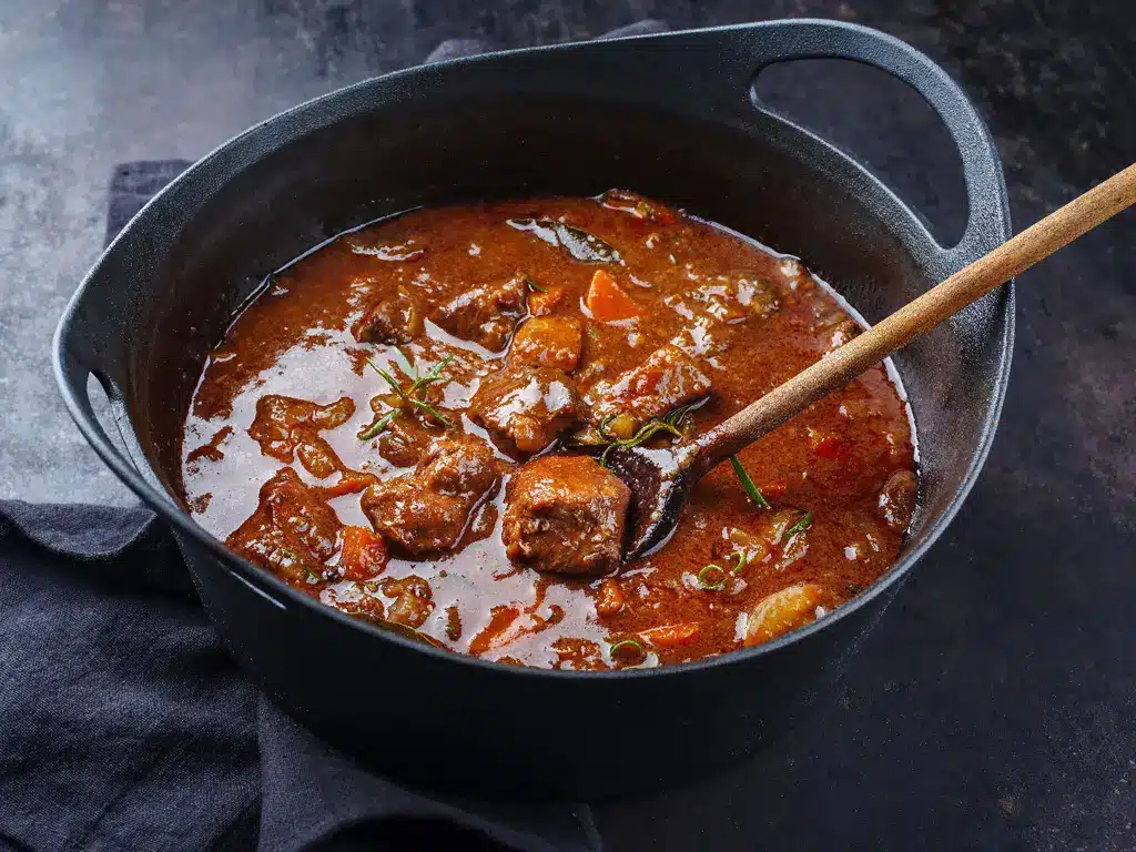 Ein Topf mit dampfendem Rindergulasch, zubereitet mit zarten Fleischstücken, Gemüse und Kräutern, in einer reichhaltigen Sauce.