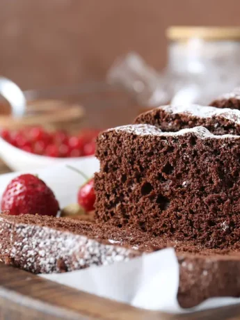 Ein saftiger Schokoladenkuchen mit Puderzucker bestreut, aufgeschnitten und dekoriert mit roten Beeren.