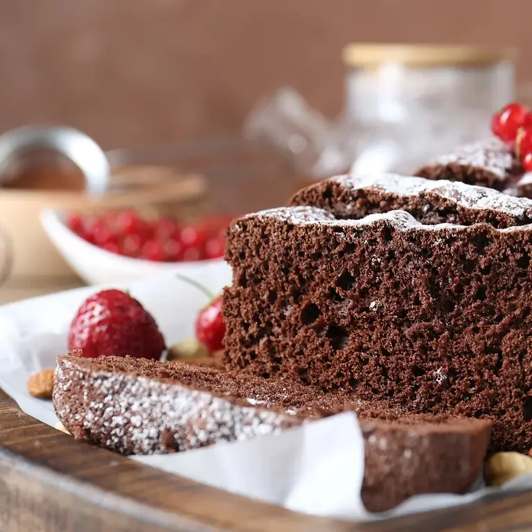 Ein saftiger Schokoladenkuchen mit Puderzucker bestreut, aufgeschnitten und dekoriert mit roten Beeren.
