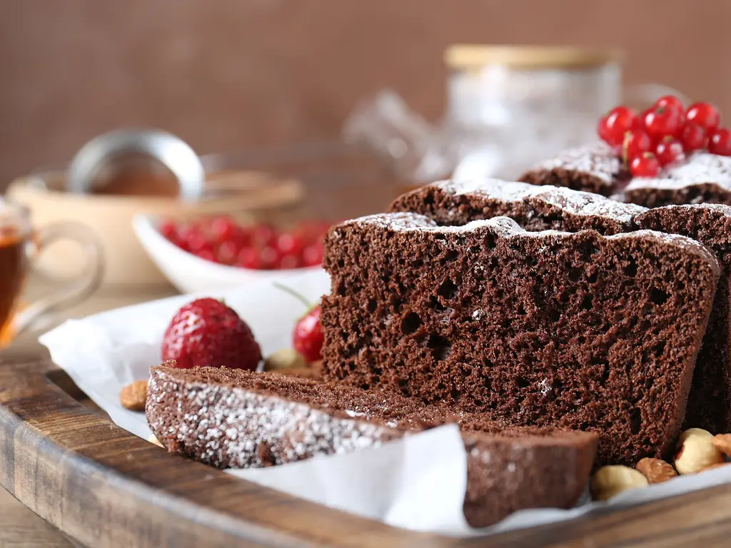 Ein saftiger Schokoladenkuchen mit Puderzucker bestreut, aufgeschnitten und dekoriert mit roten Beeren.