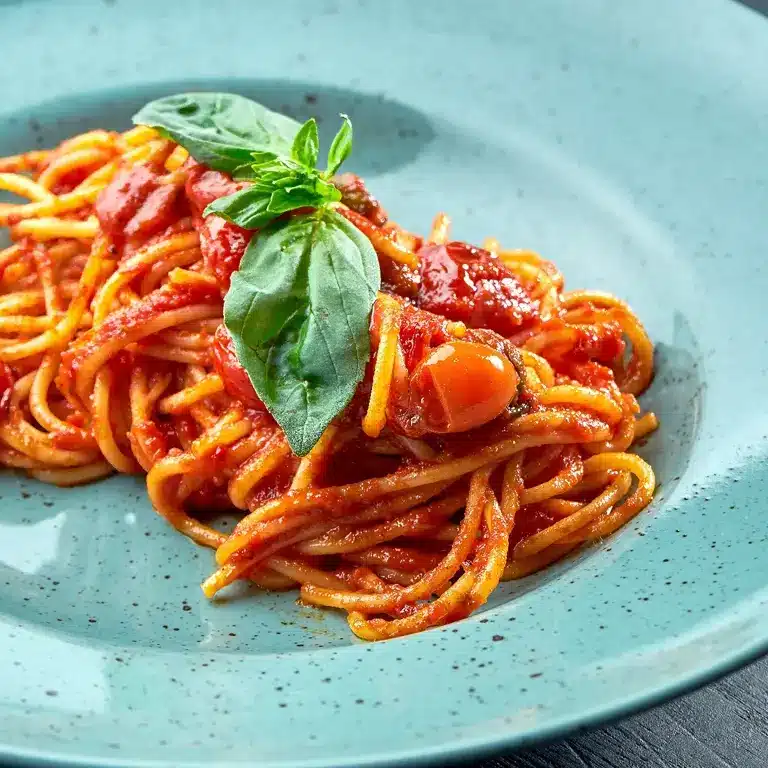 Ein Teller Spaghetti mit frischer Tomatensauce, garniert mit Basilikumblättern und Kirschtomaten.