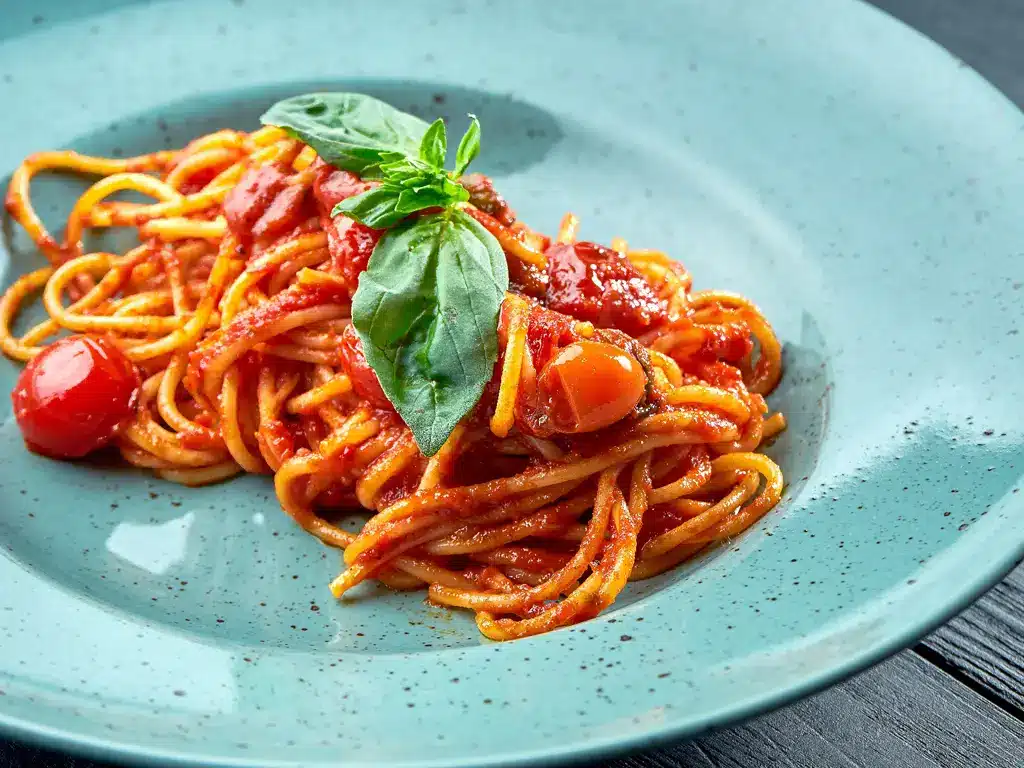 Ein Teller Spaghetti mit frischer Tomatensauce, garniert mit Basilikumblättern und Kirschtomaten.