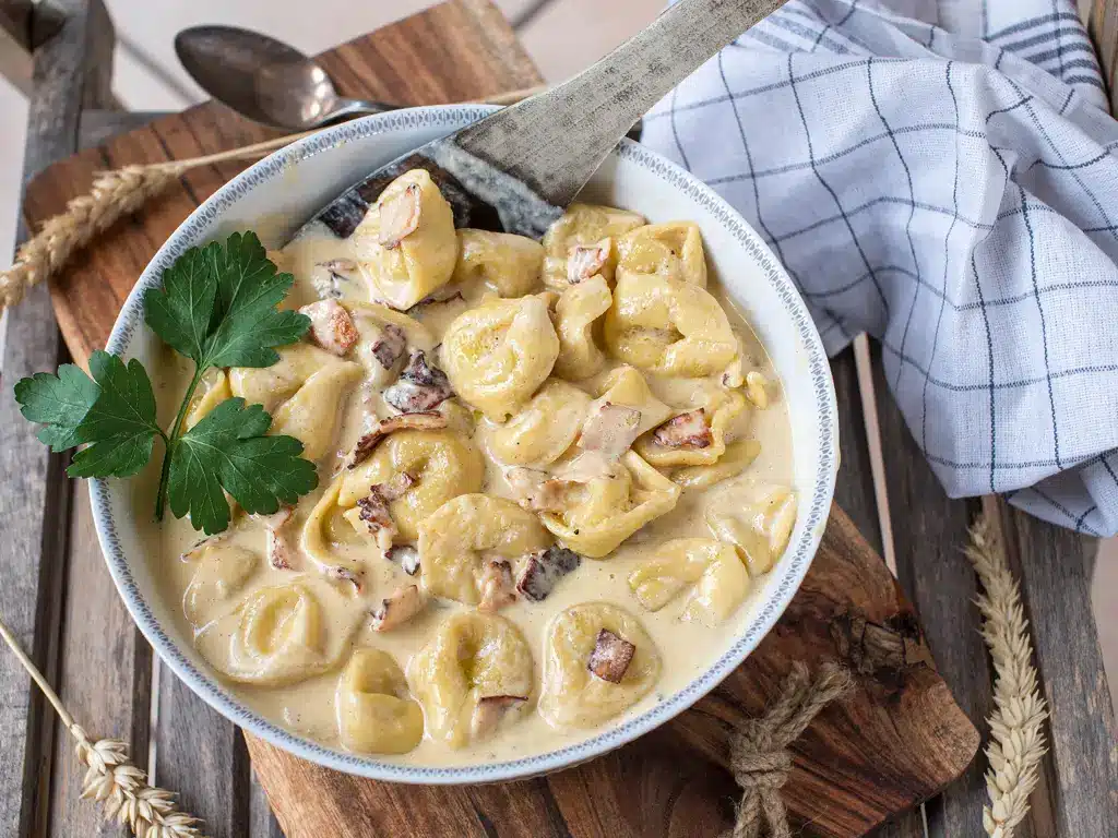 Eine Schale mit Tortellini in einer reichhaltigen, cremigen Käsesauce, garniert mit frischer Petersilie.