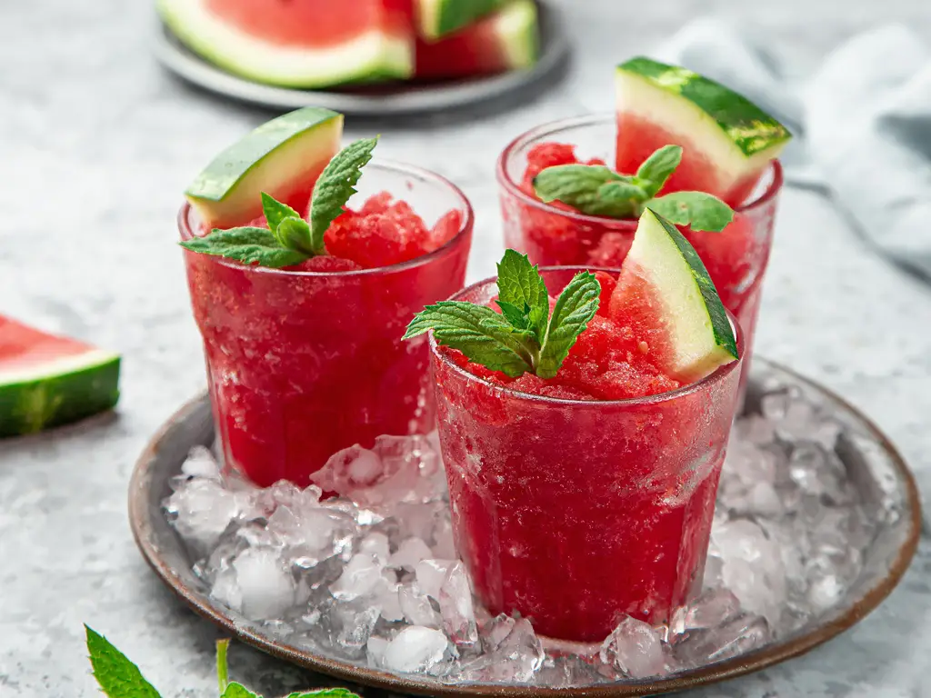 Drei Gläser mit Wassermelonen-Slush, garniert mit Minzblättern und Wassermelonenscheiben, serviert auf Eis.